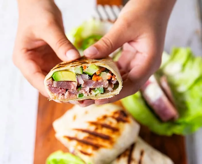 A hand holding a cut up tuna wrap showing the tuna filling with the avocado, onions and more close up