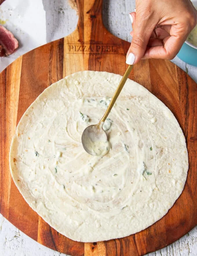 A hand spreading the sauce over the surface of the flour tortilla