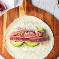 Some veggies piled over the tortilla along the middle including avocados, onions, cucumbers, carrots, and the sliced tuna on top