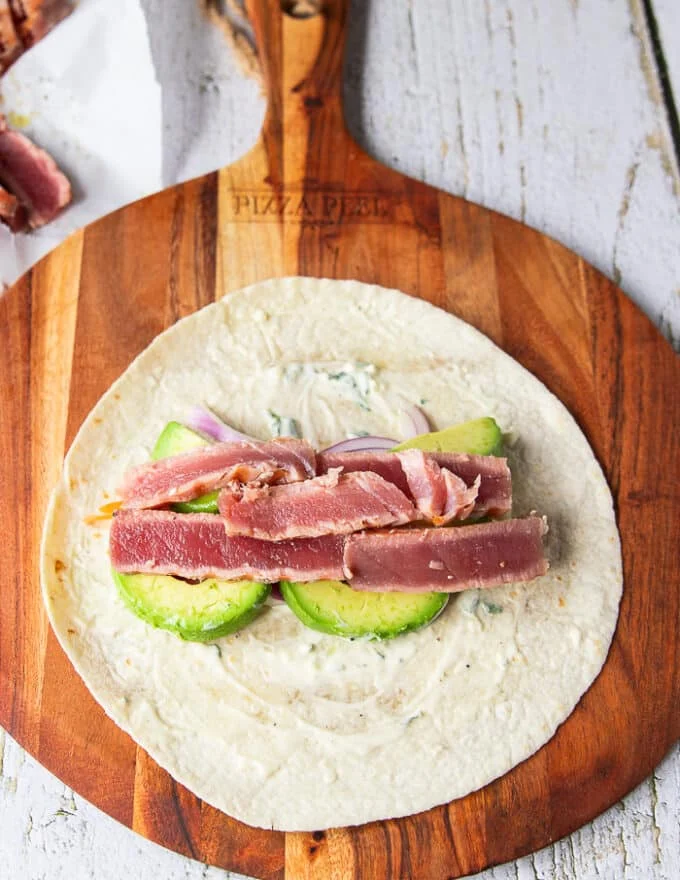 Some veggies piled over the tortilla along the middle including avocados, onions, cucumbers, carrots, and the sliced tuna on top