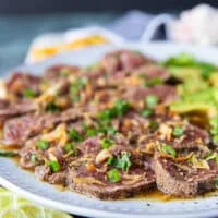 slices of beef and avocados added over the ponzu sauce and a hand sprinkling green onions and fried onions on top to finish the beef tataki