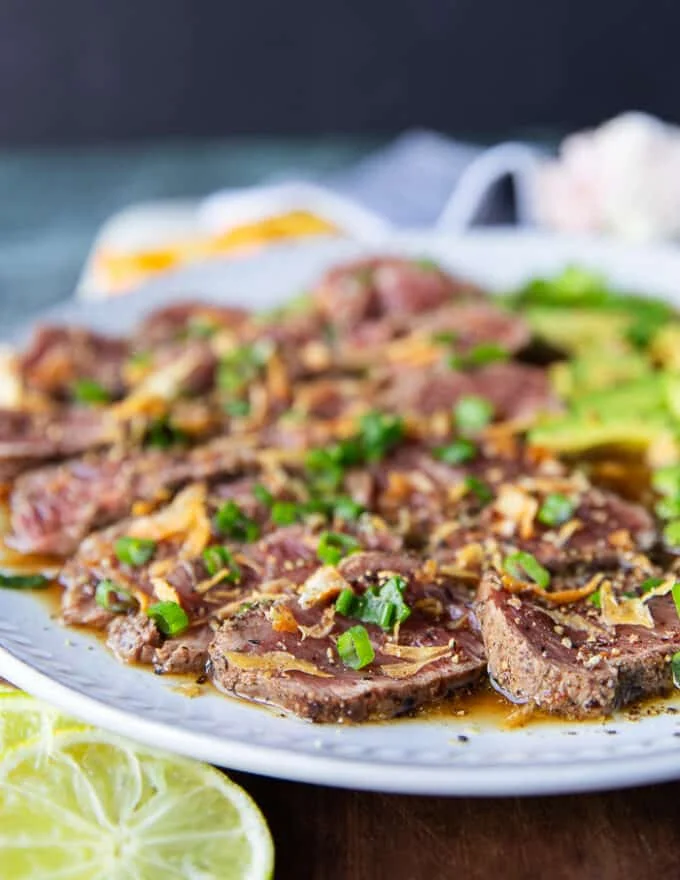 slices of beef and avocados added over the ponzu sauce and a hand sprinkling green onions and fried onions on top to finish the beef tataki
