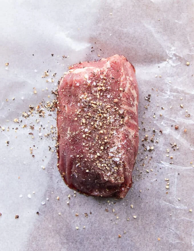 A piece of filet mignon or tenderloin seasoned with salt and pepper on parchment paper