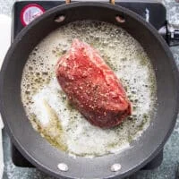 the seasoned tenderloin steak searing in butter over a hot skillet