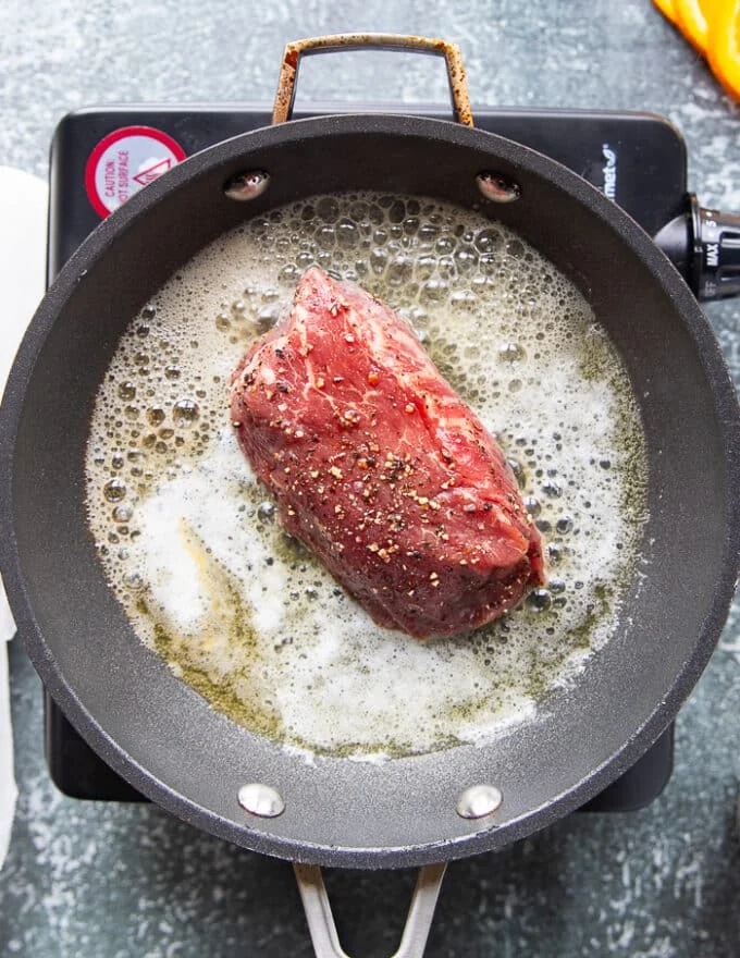 the seasoned tenderloin steak searing in butter over a hot skillet