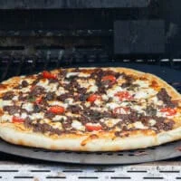 After grilling the pizza with the lid off, the lid is opened showing the golden crust and perfectly cooked grilled pizza.
