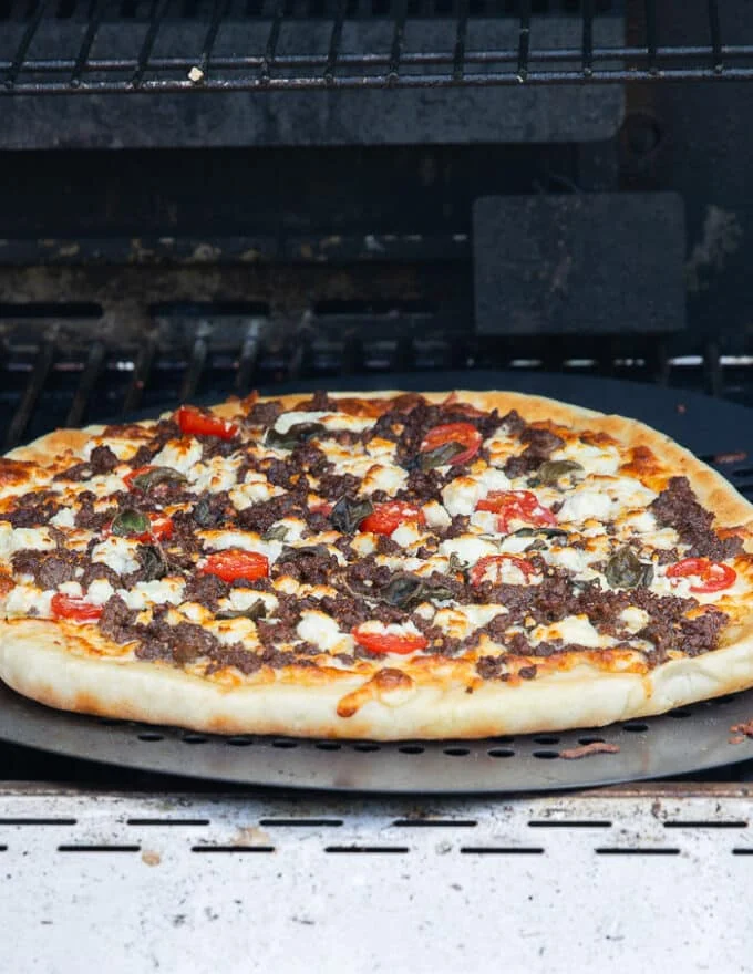 After grilling the pizza with the lid off, the lid is opened showing the golden crust and perfectly cooked grilled pizza.