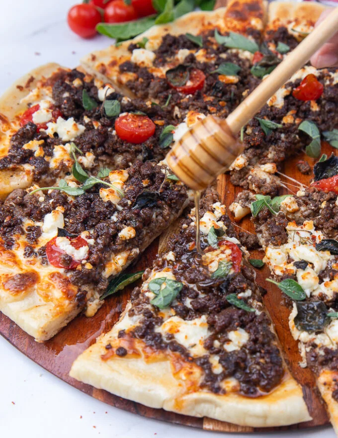 A hand drizzling some honey over the grilled pizza slice to finish off the pizza recipe