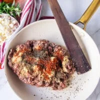 sausage ingredients all added in one skillet including the ground meat, spices and a wooden spoon mixing them