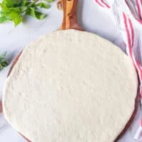 rolled out pizza dough on a wooden panel ready for the grill