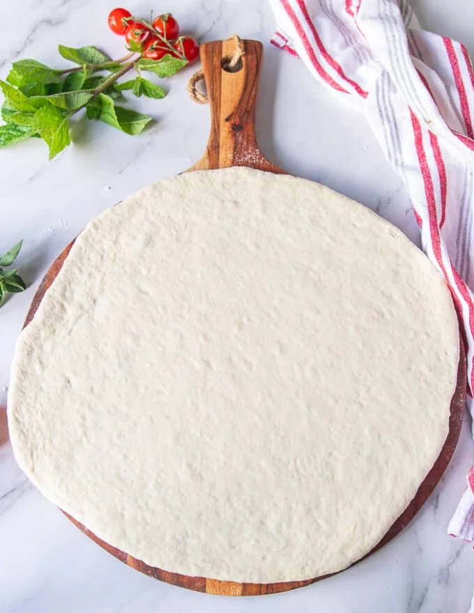 rolled out pizza dough on a wooden panel ready for the grill