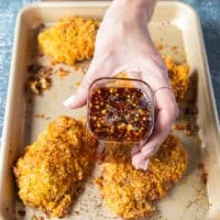 The baked chicken tenders ready and out of the oven golden and crispy, and a hand holding some hot honey ready to pour over