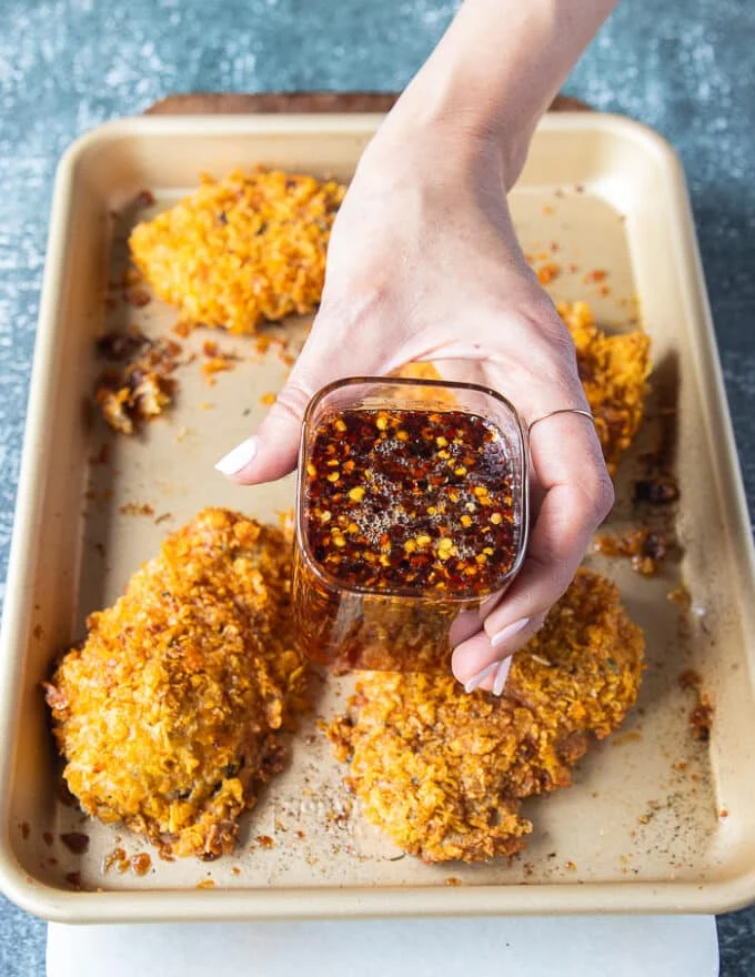 The baked chicken tenders ready and out of the oven golden and crispy, and a hand holding some hot honey ready to pour over