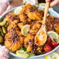 the hot honey chicken tenders arranged in a plate and hand pouring in a spoonful of hot honey on top