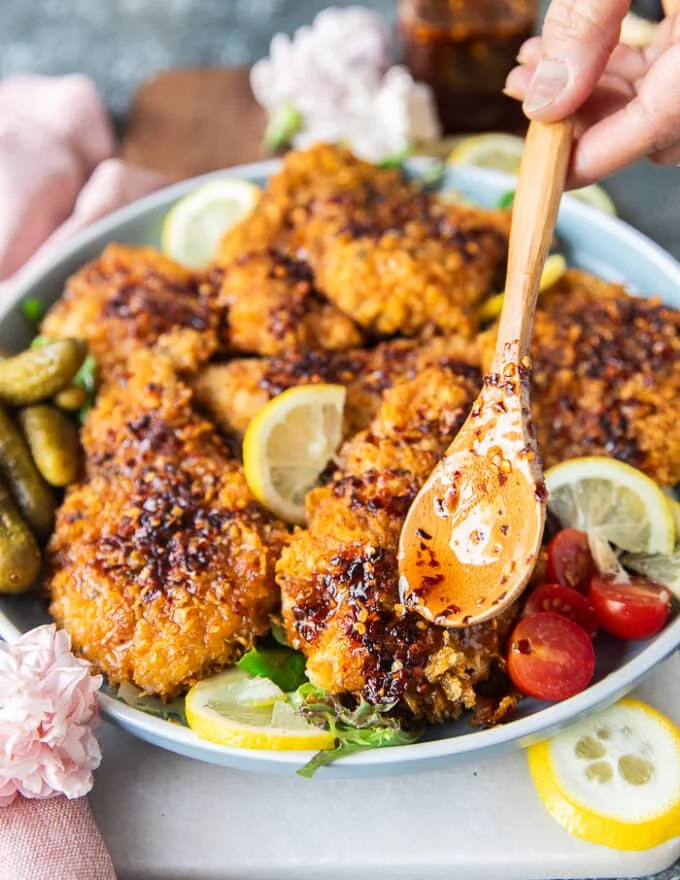 the hot honey chicken tenders arranged in a plate and hand pouring in a spoonful of hot honey on top