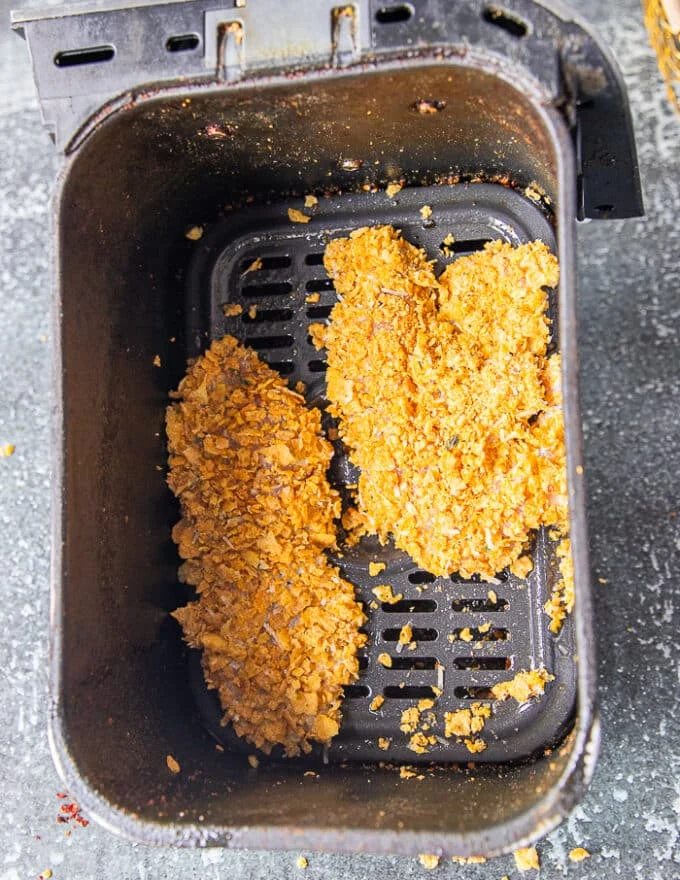 chicken tenders with cornflakes coating in an air fryer basked sprayed with oil ready to air fry