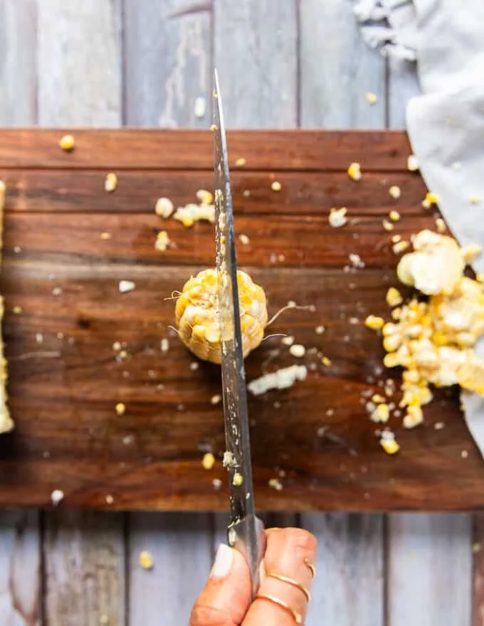 The corn standing up right on the board and a knife used to cut down the half