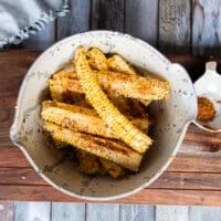 A bowl of corn ribs and chilli power seasoning and oil and the ribs are tossed and coated