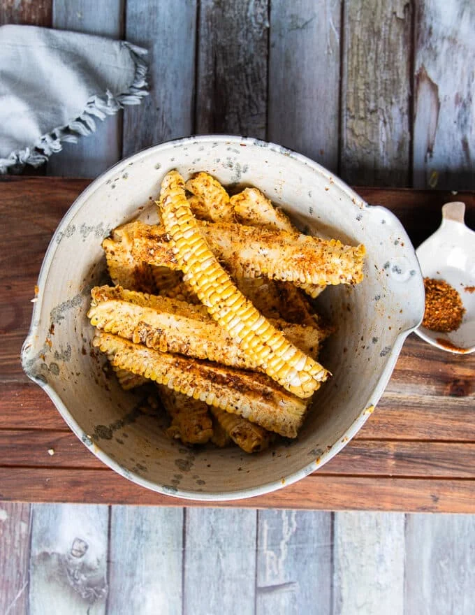A bowl of corn ribs and chilli power seasoning and oil and the ribs are tossed and coated