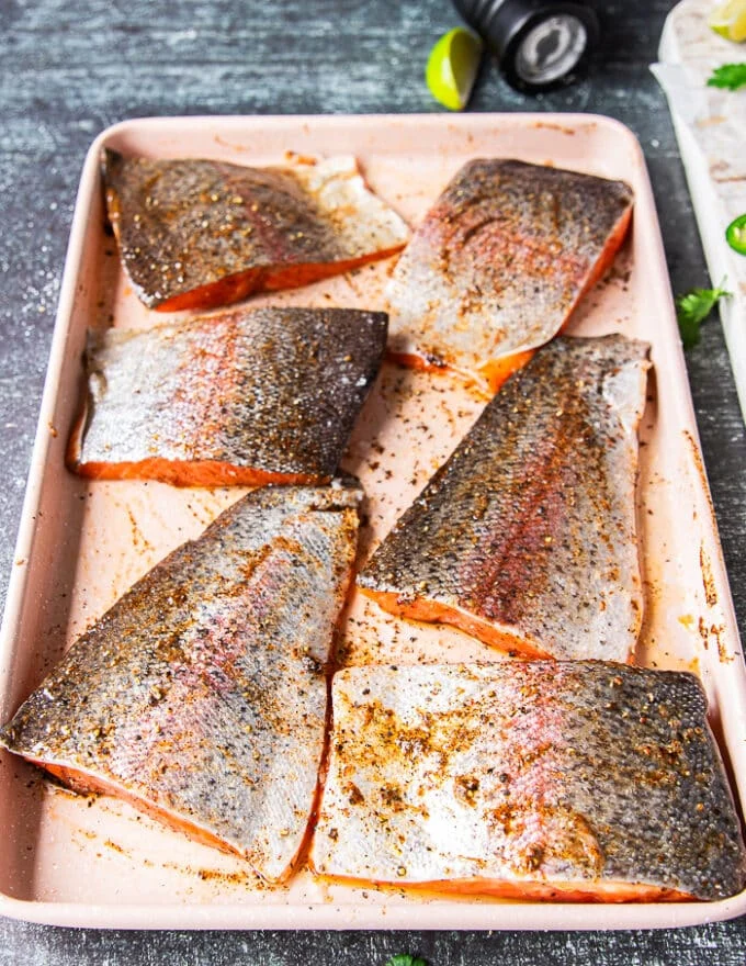 heavily oiled and seasoned rainbow trout fillets on a sheet ready to grill
