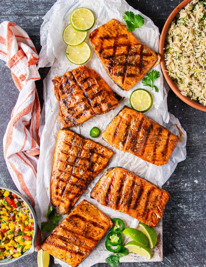 A platter of grilled trout on a wooden board showing the grilled trout over the BBQ and the grilled trout in a grill basket