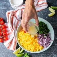 A hand pouring the lime juice over the plate of mango pico de gallo ingredients