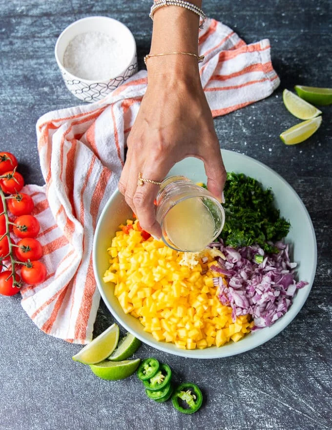 A hand pouring the lime juice over the plate of mango pico de gallo ingredients