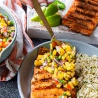 A hand spooning some mango pico de gallo over some grilled salmon fillets