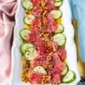 tuna crudo on a plate with sliced cucumbers, a citrus dressing, capers , lots of olive oil and fried garlic