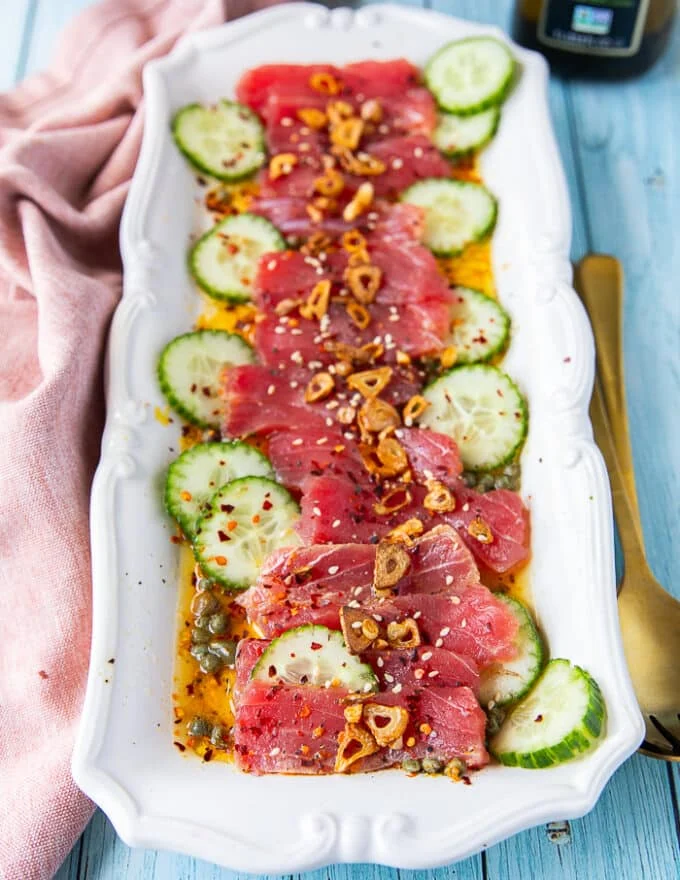 tuna crudo on a plate with sliced cucumbers, a citrus dressing, capers , lots of olive oil and fried garlic