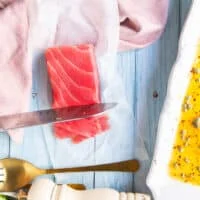 A hand holding a sharp knife thinly slicing the saku tuna into thin slices for the tuna crudo