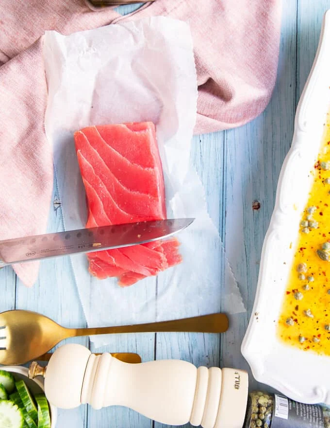 A hand holding a sharp knife thinly slicing the saku tuna into thin slices for the tuna crudo