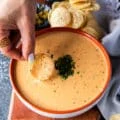 Close up of a hand scooping some queso with a tortilla chip showing the luscious texture of the dip