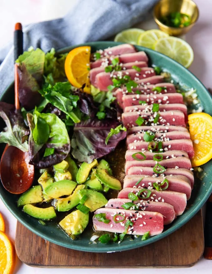 A plate of tuna tataki served over ponzu sauce and with avocados on the side