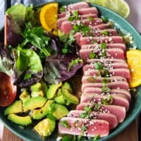 the tuna slices arranged over the ponzu sauce surroounde dby some avocado slices, garnished with scallions and sesame seeds and ready to serve