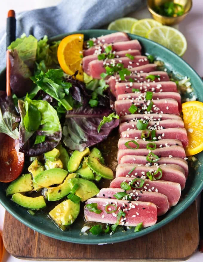 the tuna slices arranged over the ponzu sauce surroounde dby some avocado slices, garnished with scallions and sesame seeds and ready to serve