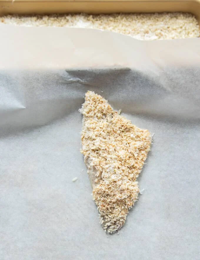 Fully coated perch fish placed on a parchment lined baking sheet
