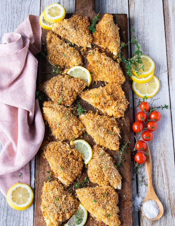A board with the cooked perch fillets arranged on it for serving with sides of sauces, lemon wedges and a tea towel