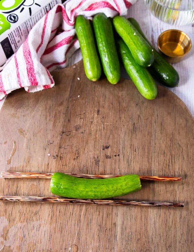 A cucumber is placed on top of two chopsticks on a cutting board