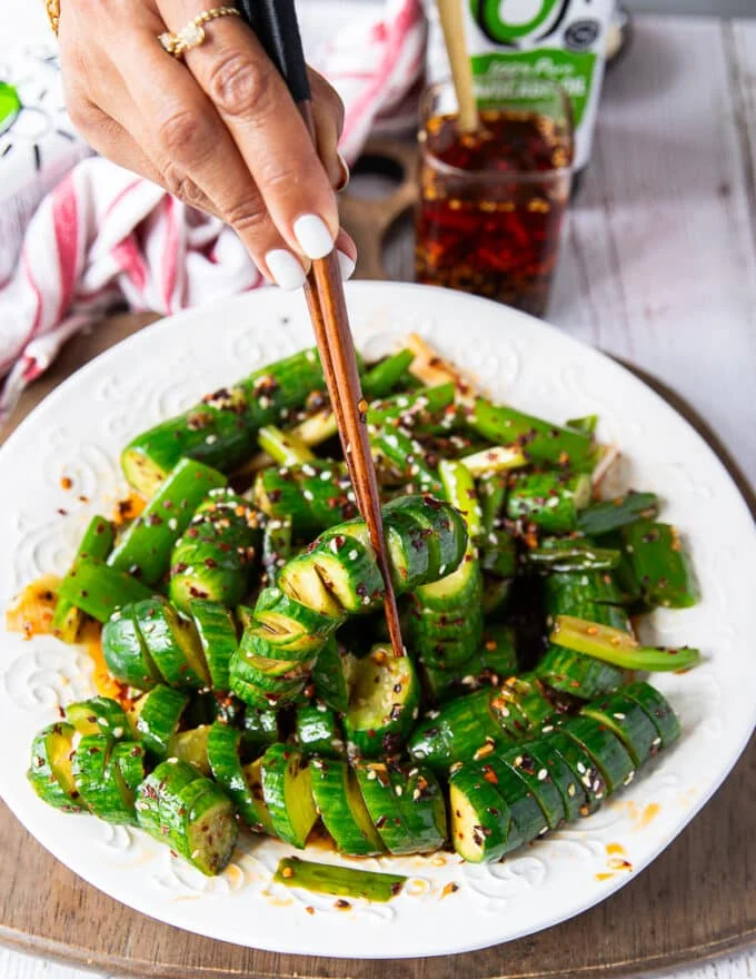 A hand holding two chopsticks and eating the Asian cucumber salad showing the spiral cucumbers dressed up