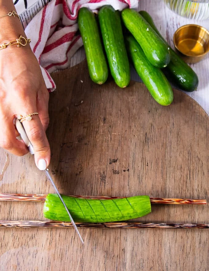 A hand holding a paring knife and making slits along the cucumber 1/4 inch apart on a 45 degree angle