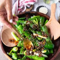 A hand pouring the chili oil and remaining ingredients over the cucumbers to make asian cucumber salad