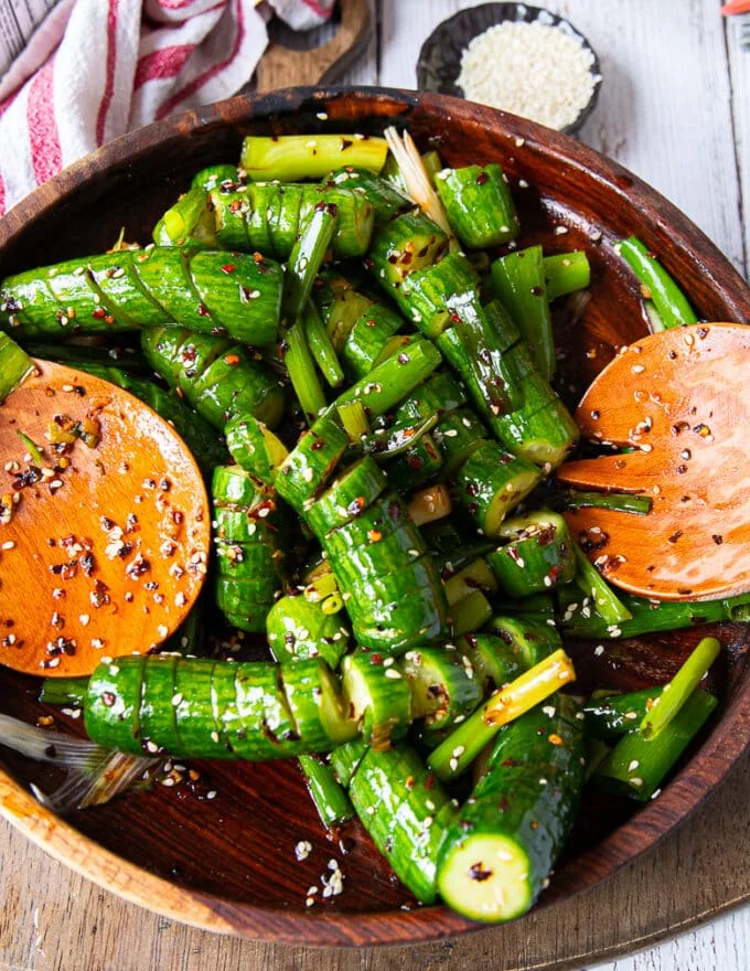 Tow spoons tossing the asian cucumber salad together with the dressing