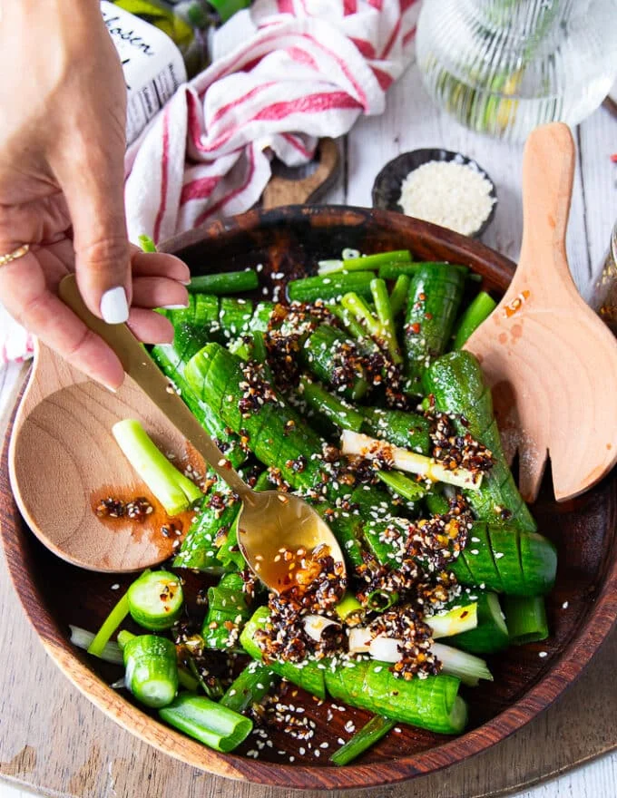 A hand spooning some chili oil over an asian cucumber salad