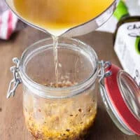 a hand pouring the hot oil carefully and slowly into the jar as it the oil begins ti bubble