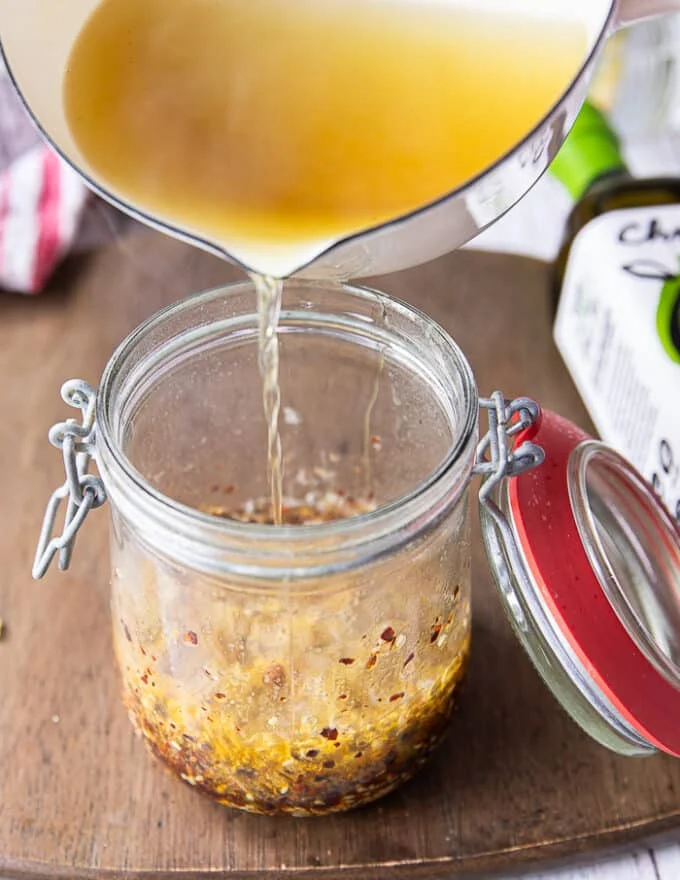 a hand pouring the hot oil carefully and slowly into the jar as it the oil begins ti bubble
