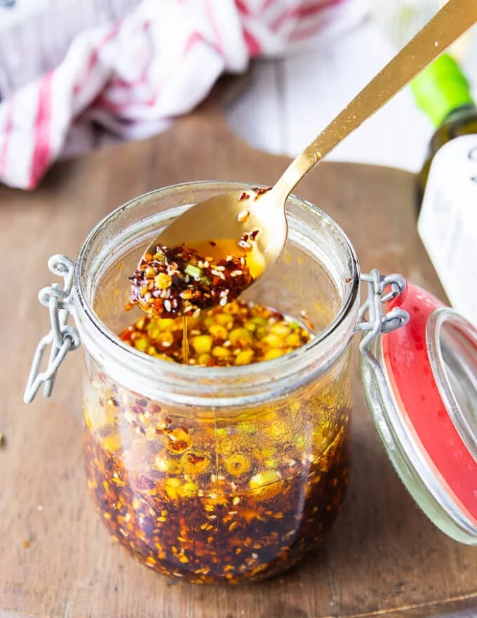 A spoon scooping some chili oil from a jar showing the chillies, garlic and all ingredients well blended into the oil