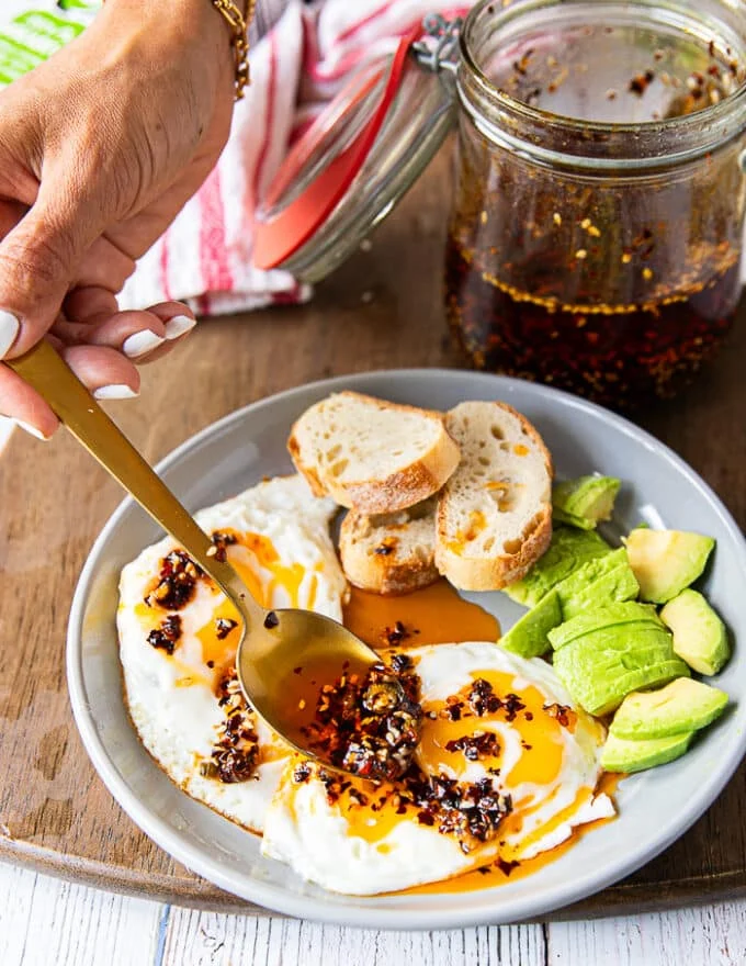 A hand spooning some chili oil over sunny side up eggs
