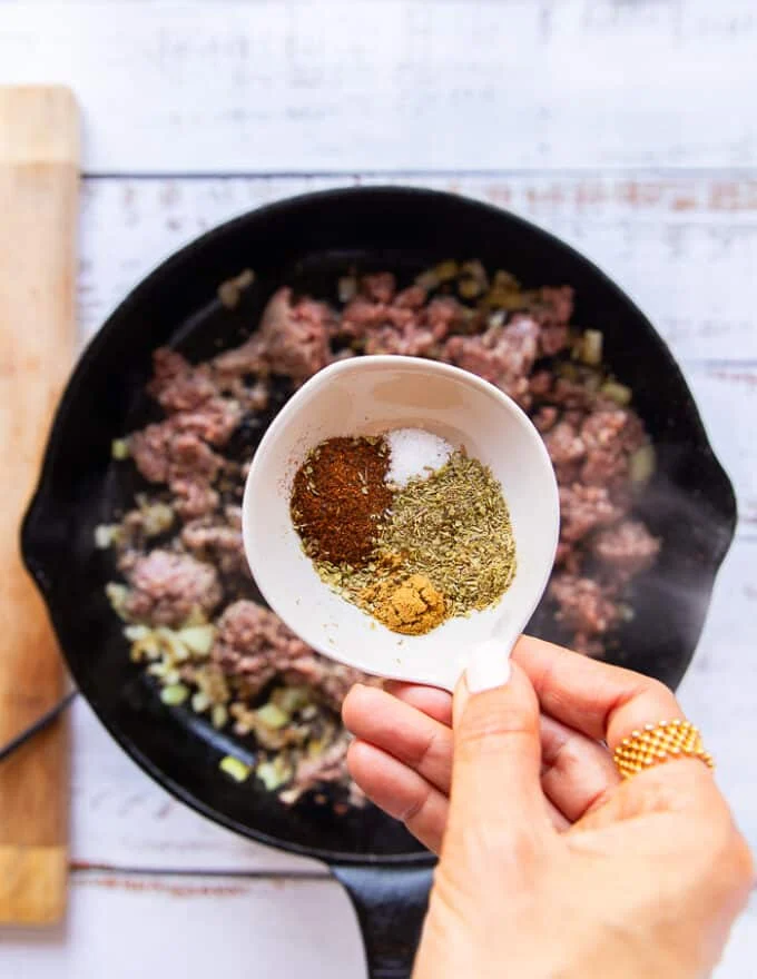 ground beef and onion cooking in a skillet and then a hand holding the taco spice mix ready to season the mixture