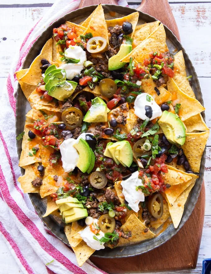 loaded plate of ground beef nachos with salsa, avocado, guacamole, sour cream, pickled jalapenos, green onions and black olives